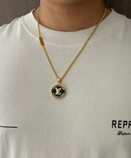 Gold-tone necklace with round logo pendant worn on a white crewneck shirt