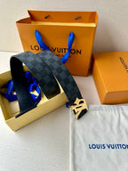 Dark patterned leather belt with LV logo buckle and matching gift bag behind.