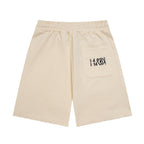 Light beige Maison Margiela shorts with drawstring and logo graphic on front pocket.
