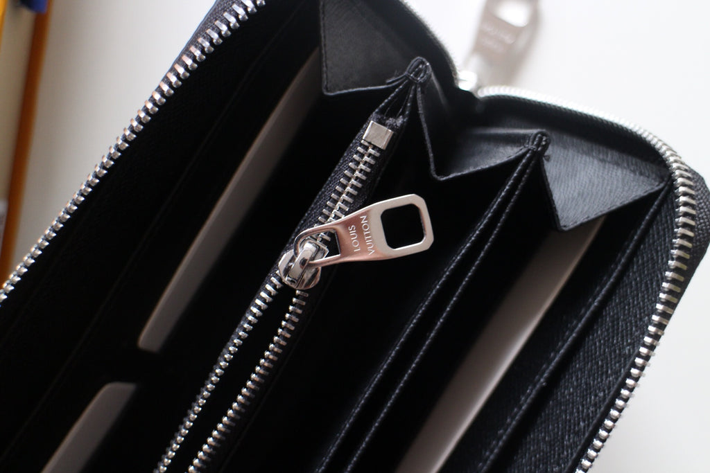 Small Louis Vuitton zip wallet open with zipper pull and multiple card slots visible.