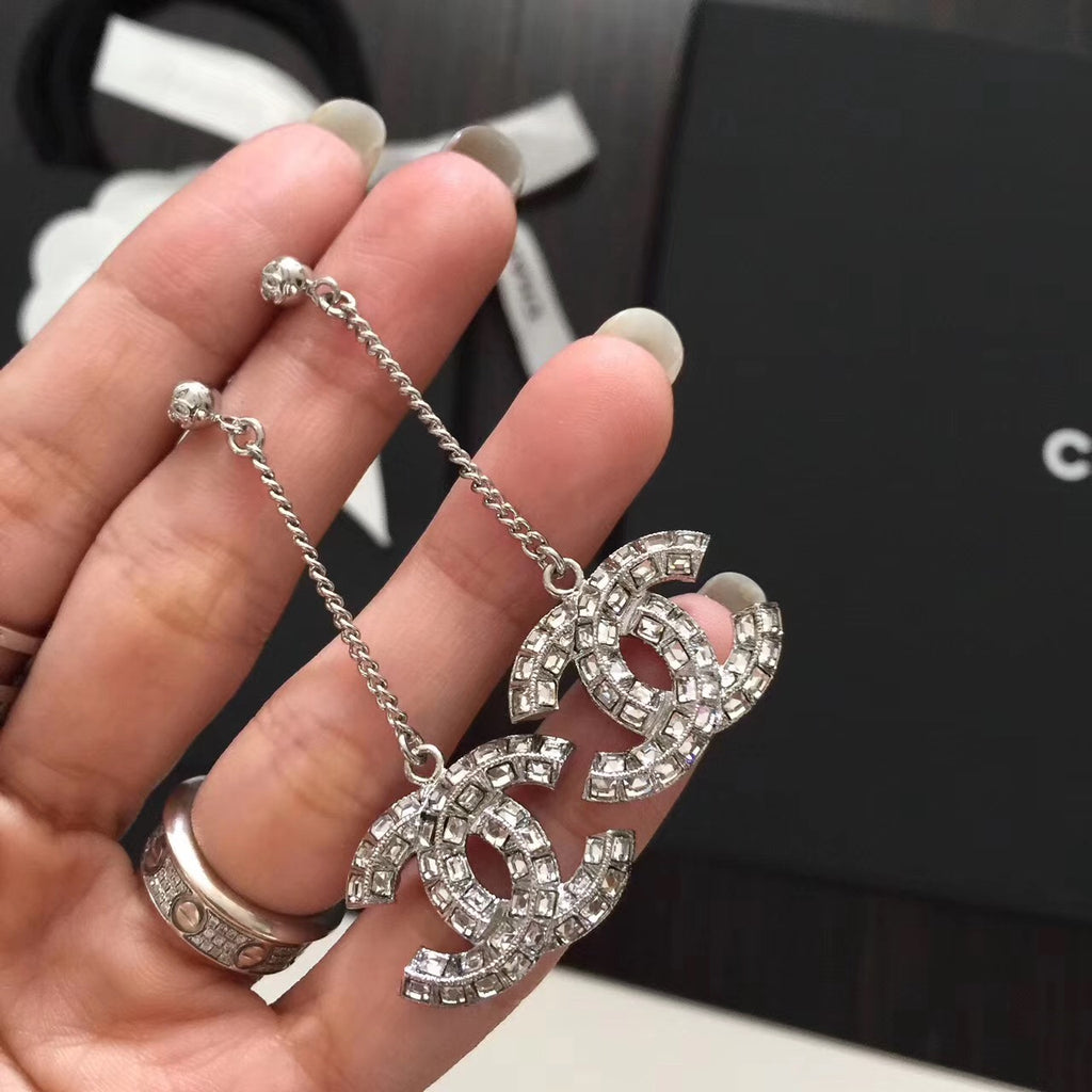 Rhinestone Chanel logo drop earrings with silver-tone chains, held in hand