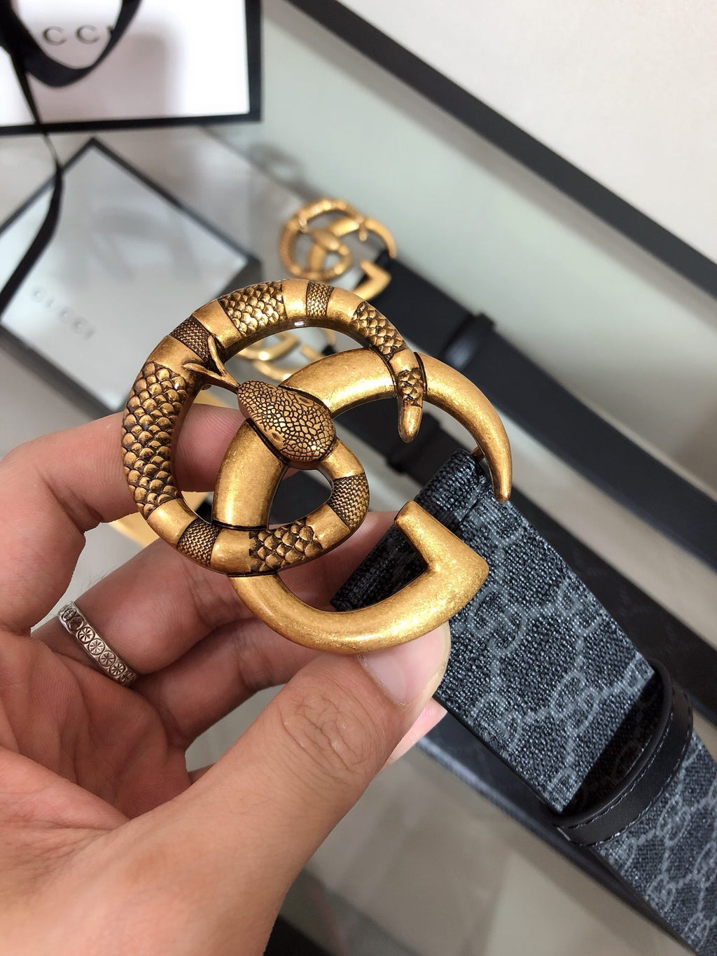 Belt buckle close-up: gold ring with snakeskin-style trim on black strap