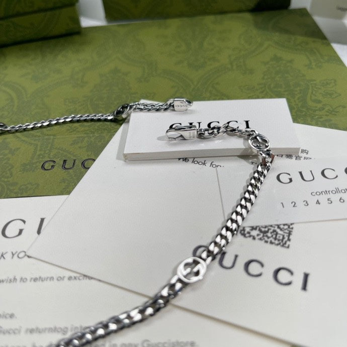 Silver-tone chain necklace with round pendant and logo charm, close-up