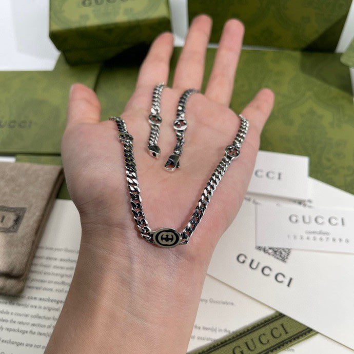 Silver-tone chain necklace on hand, round logo pendant and chain links visible