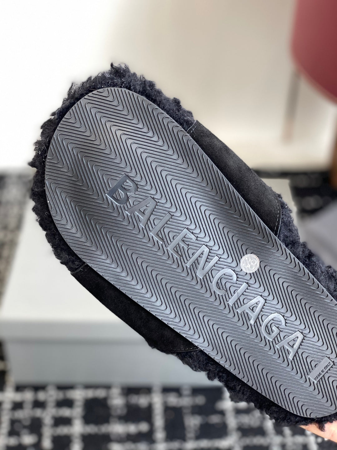 Black fuzzy slide sandal outsole with embossed logo pattern, close-up
