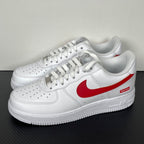 White low-top sneakers with red Nike swoosh and Supreme logo, front side view, lace-up.