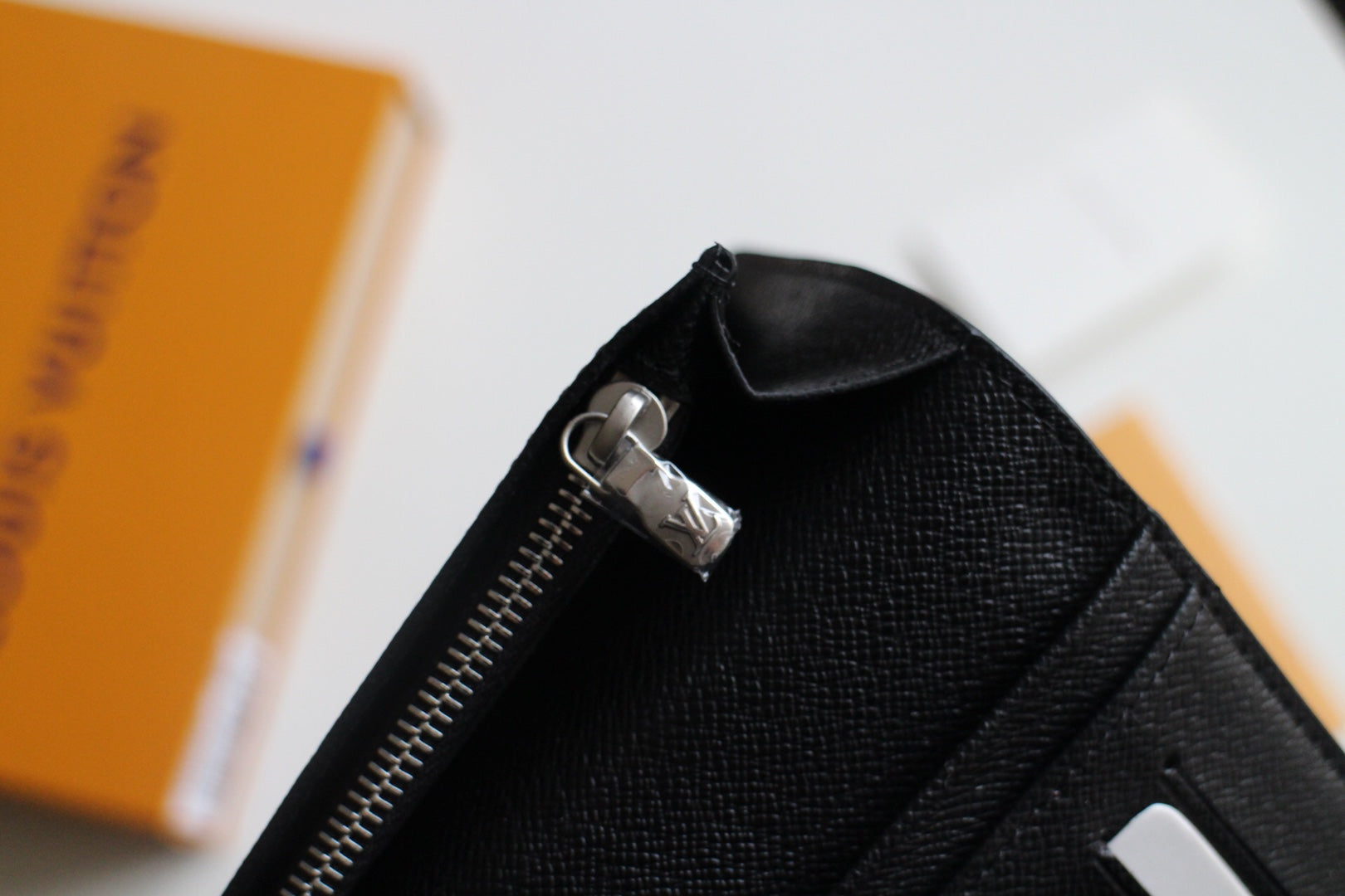 Louis Vuitton small wallet zipper pull on black leather, open edge visible