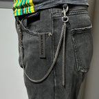 Silver-tone chain keychain hanging on dark jeans with label showing