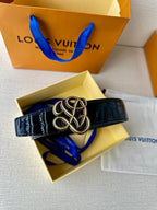 Dark navy croc belt with gold-tone interlaced buckle, laid over box