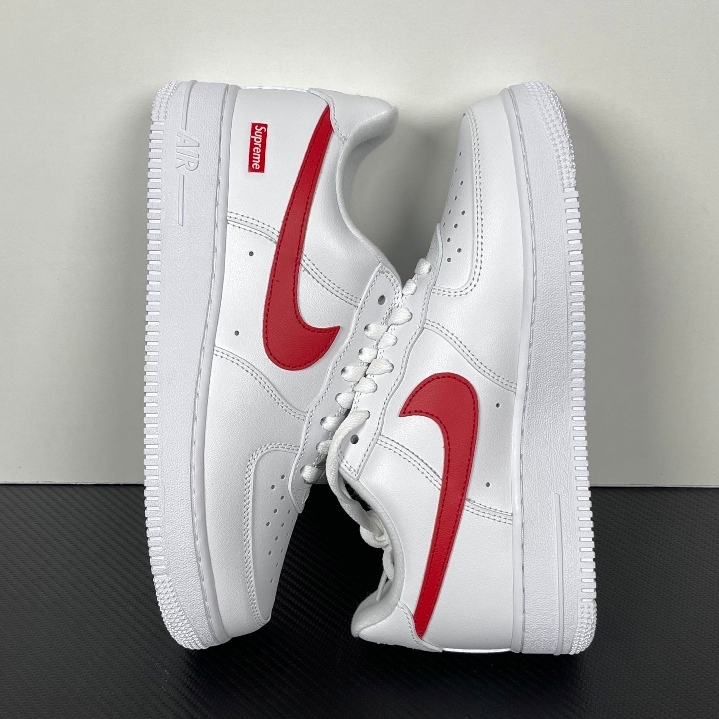 White low-top sneakers with red swoosh and Supreme heel patch, angled side view.