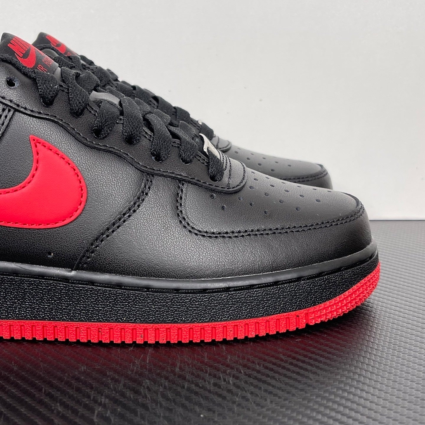 Black low-top sneaker with red swoosh, perforated toe, and black laces