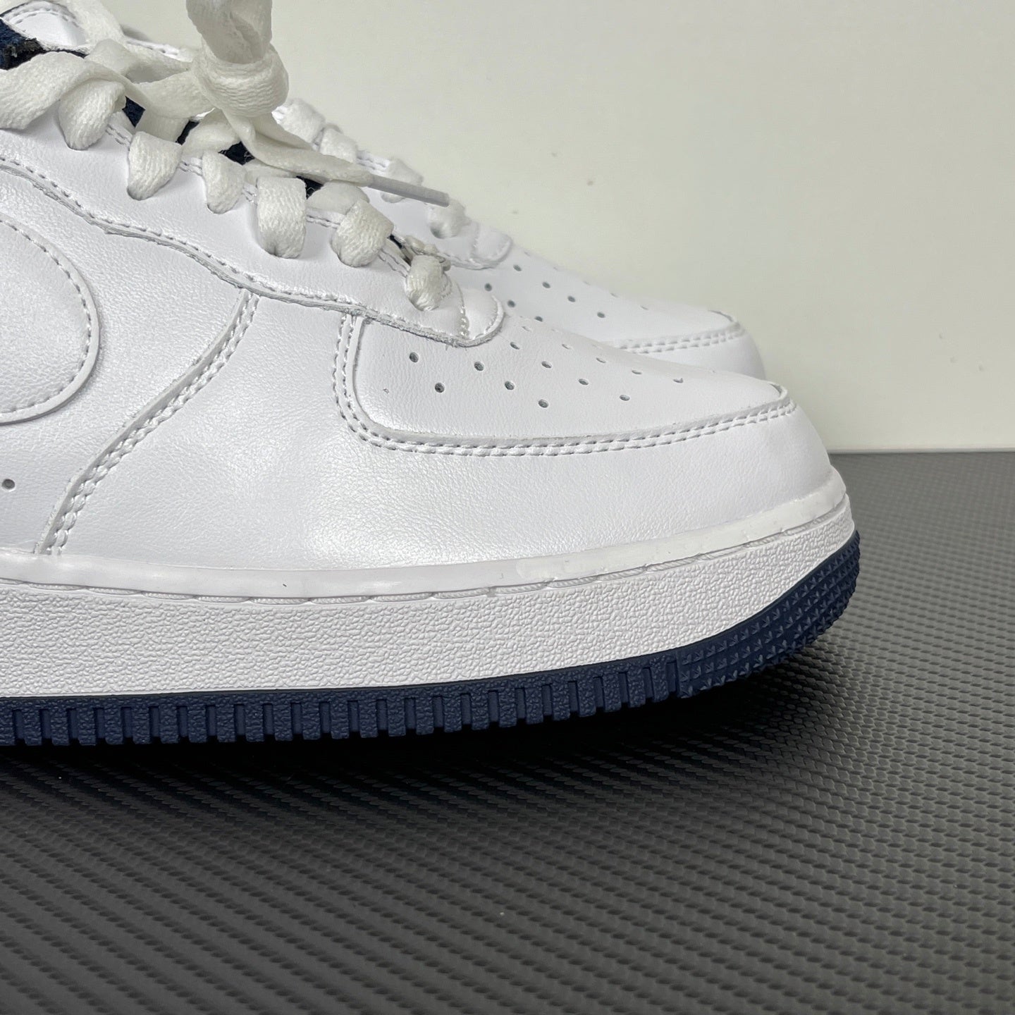 White Nike Air Force 1 low-top sneaker with perforated toe and navy outsole edge