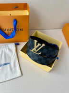 Belt on display with dark checkered strap and gold-tone LV buckle, adjustable punched holes