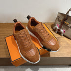 Brown suede lace-up sneakers on orange box, showing white sole and paneled stitching