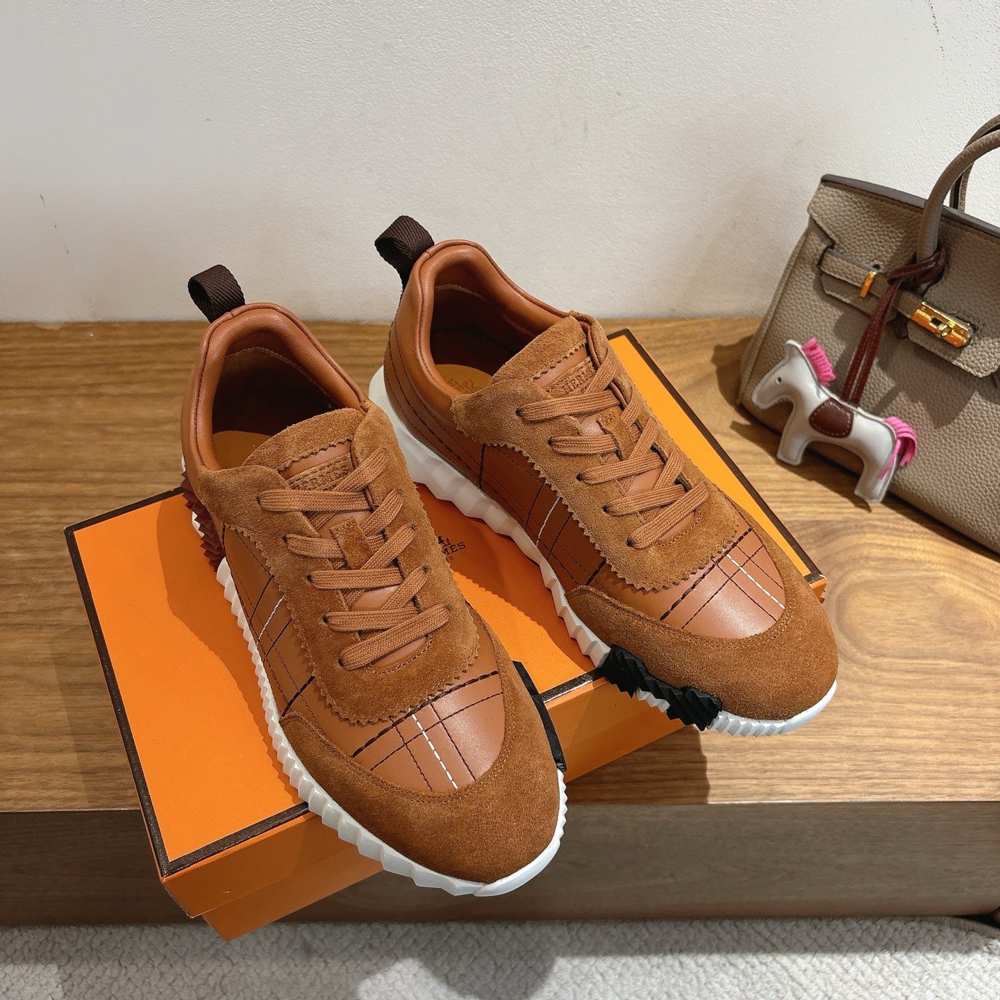Brown suede lace-up sneakers on orange box, showing white sole and paneled stitching