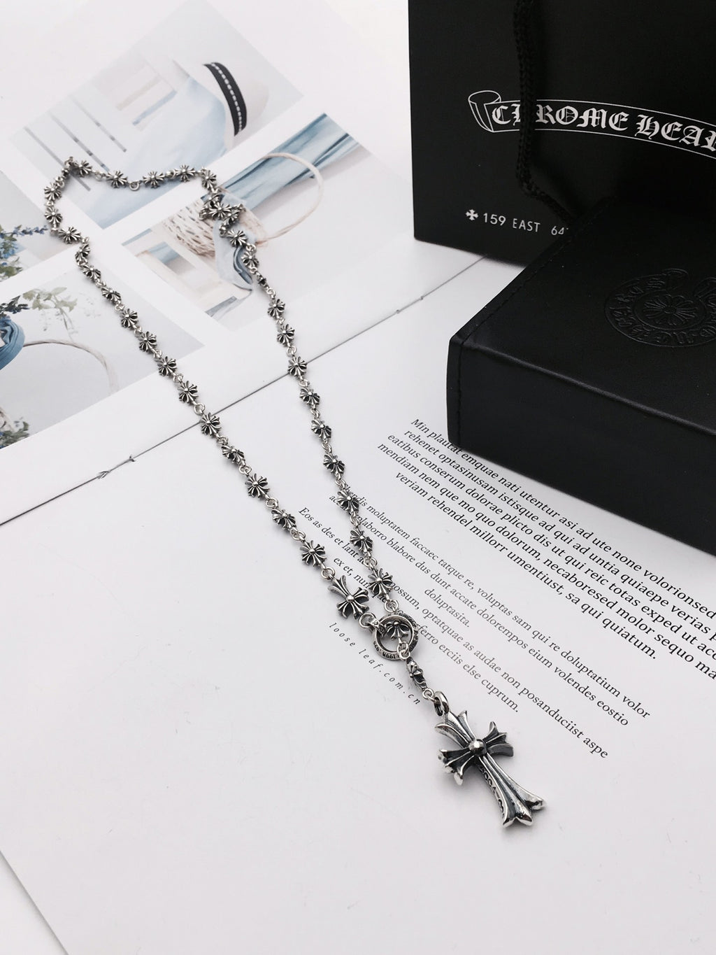 Silver-tone chain necklace with cross pendant on a black-and-white box