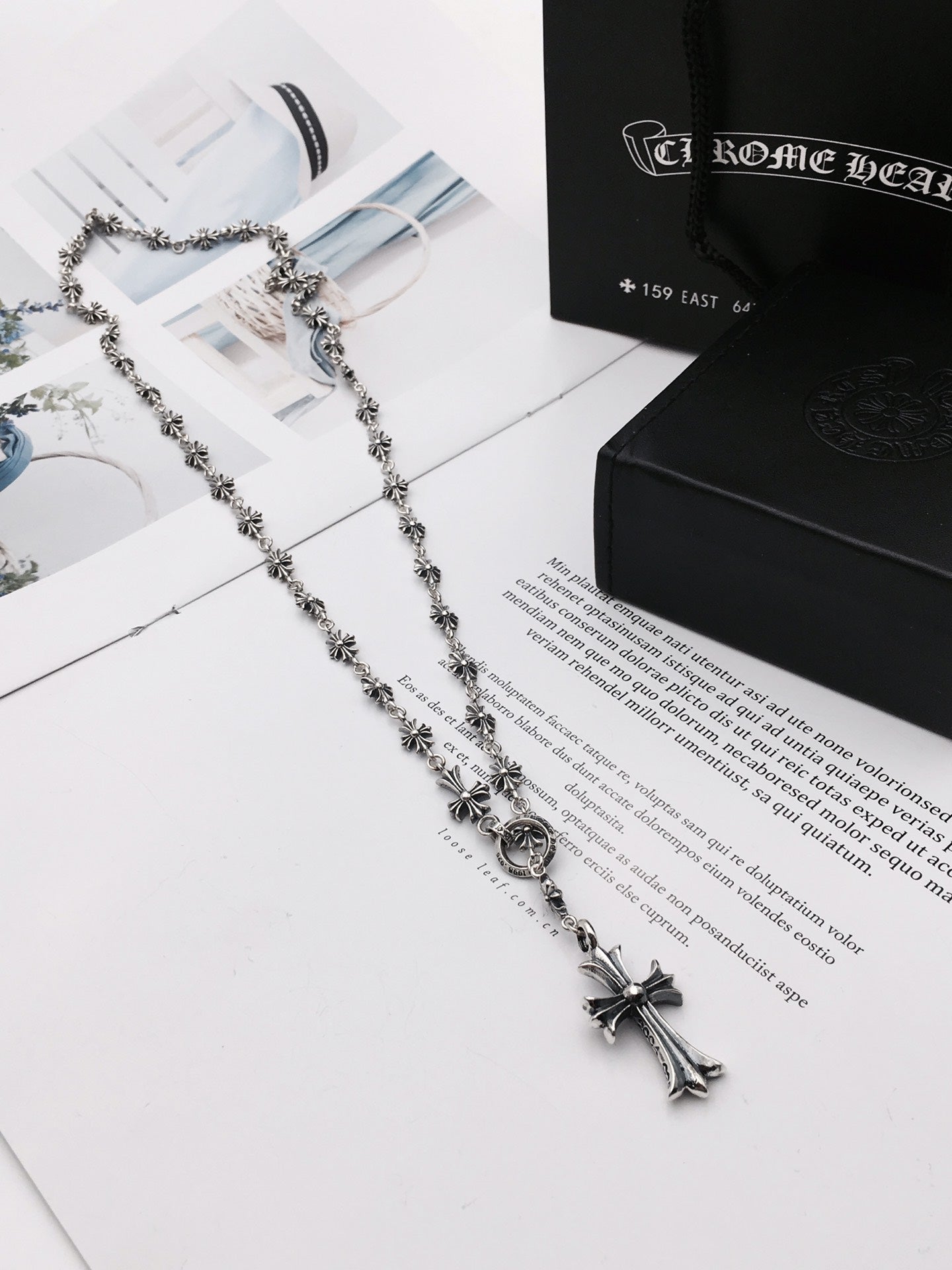 Silver-tone chain necklace with cross pendant on a black-and-white box