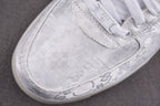 Close-up of white low-top sneakers with lace panel and embossed logos