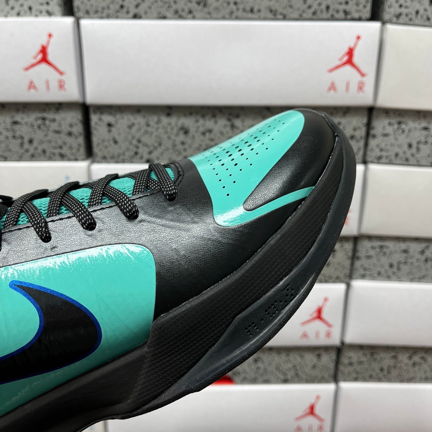 Close-up of black and teal sneaker side with blue swoosh and teal paneling.