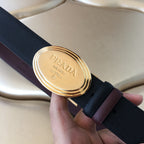 Prada belt close-up of gold oval buckle on dark strap with brown keeper.