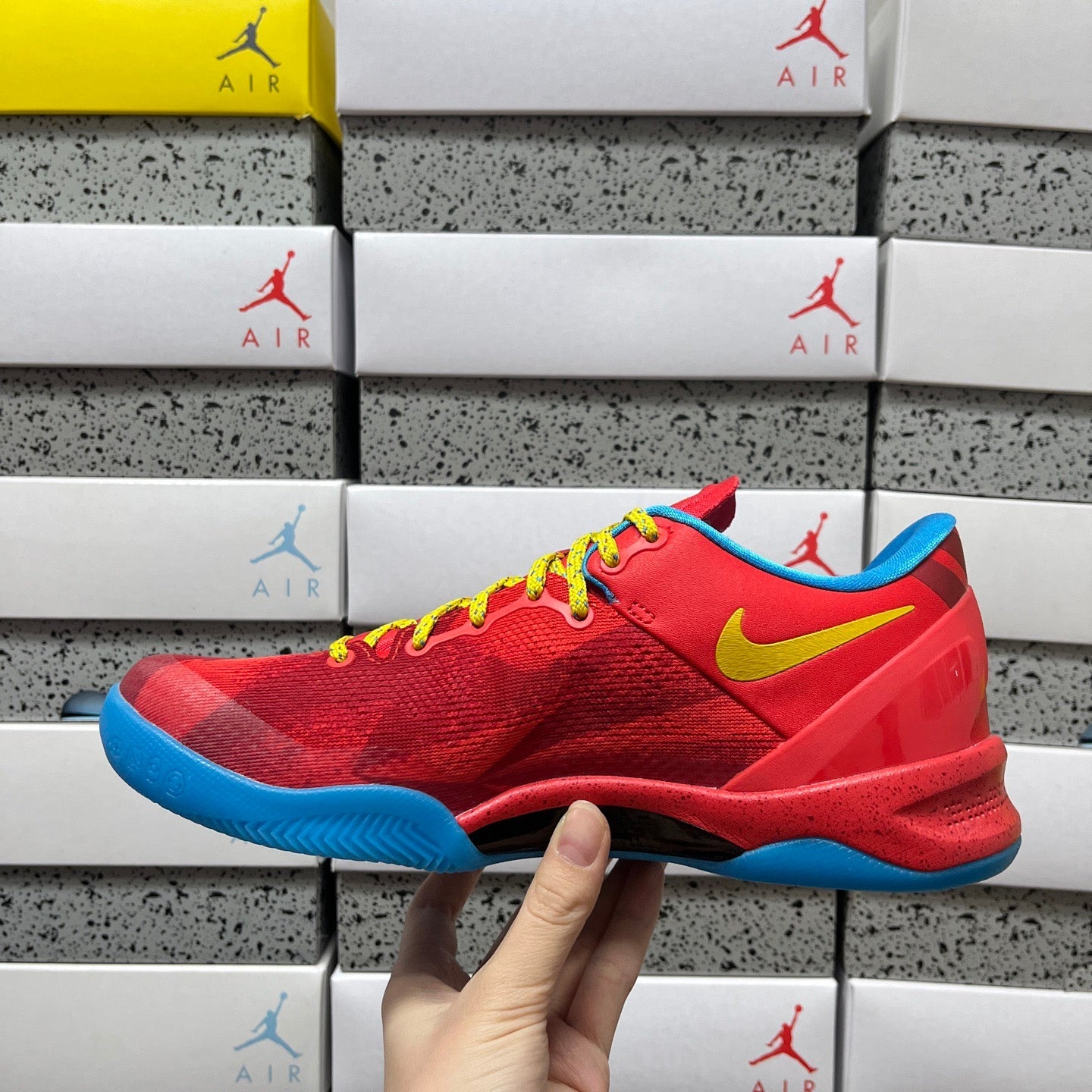 Red lace-up sneaker with yellow swoosh, blue sole, and textured upper.