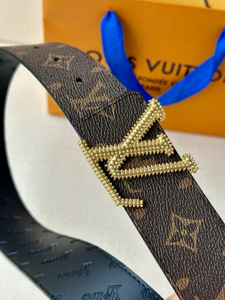 Dark monogram belt close-up with ornate gold buckle and crystal-like trim