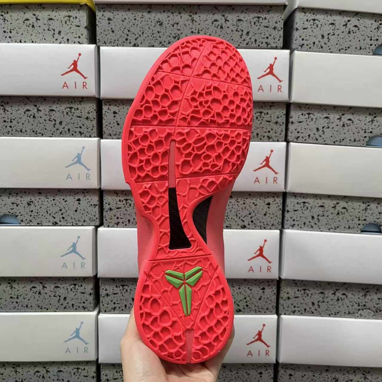 Red rubber outsole with textured tread and green bow logo at heel