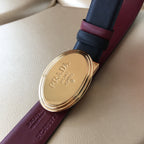 Designer belt with burgundy underside and navy top strap, featuring oval gold buckle