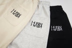 Front pocket view of Maison Margiela shorts in beige, gray, and black with logo print.