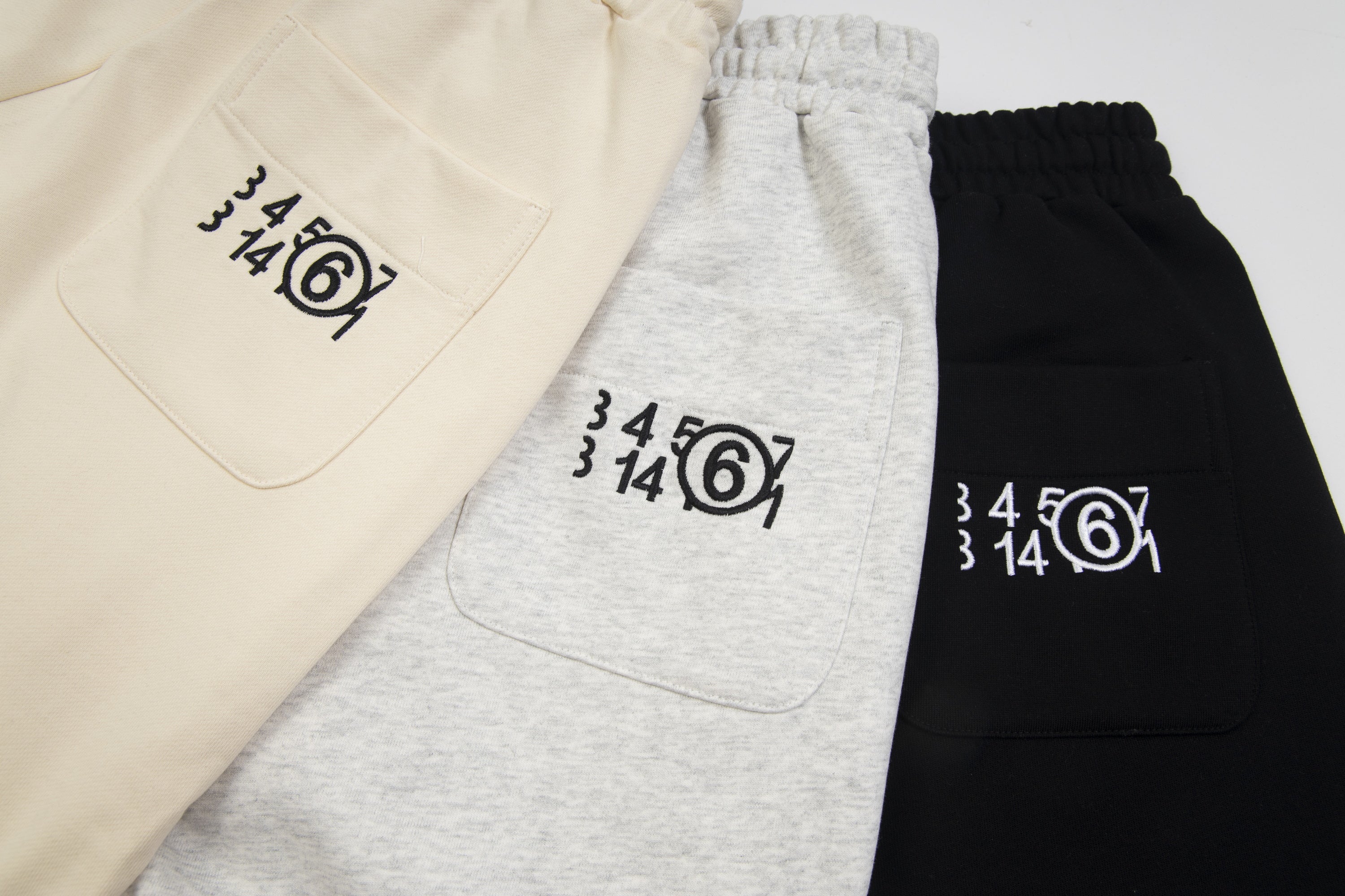Front pocket view of Maison Margiela shorts in beige, gray, and black with logo print.
