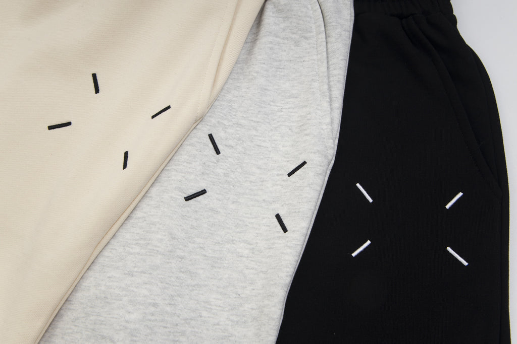 Side view of Maison Margiela shorts in beige, heather gray, and black with dash artwork.