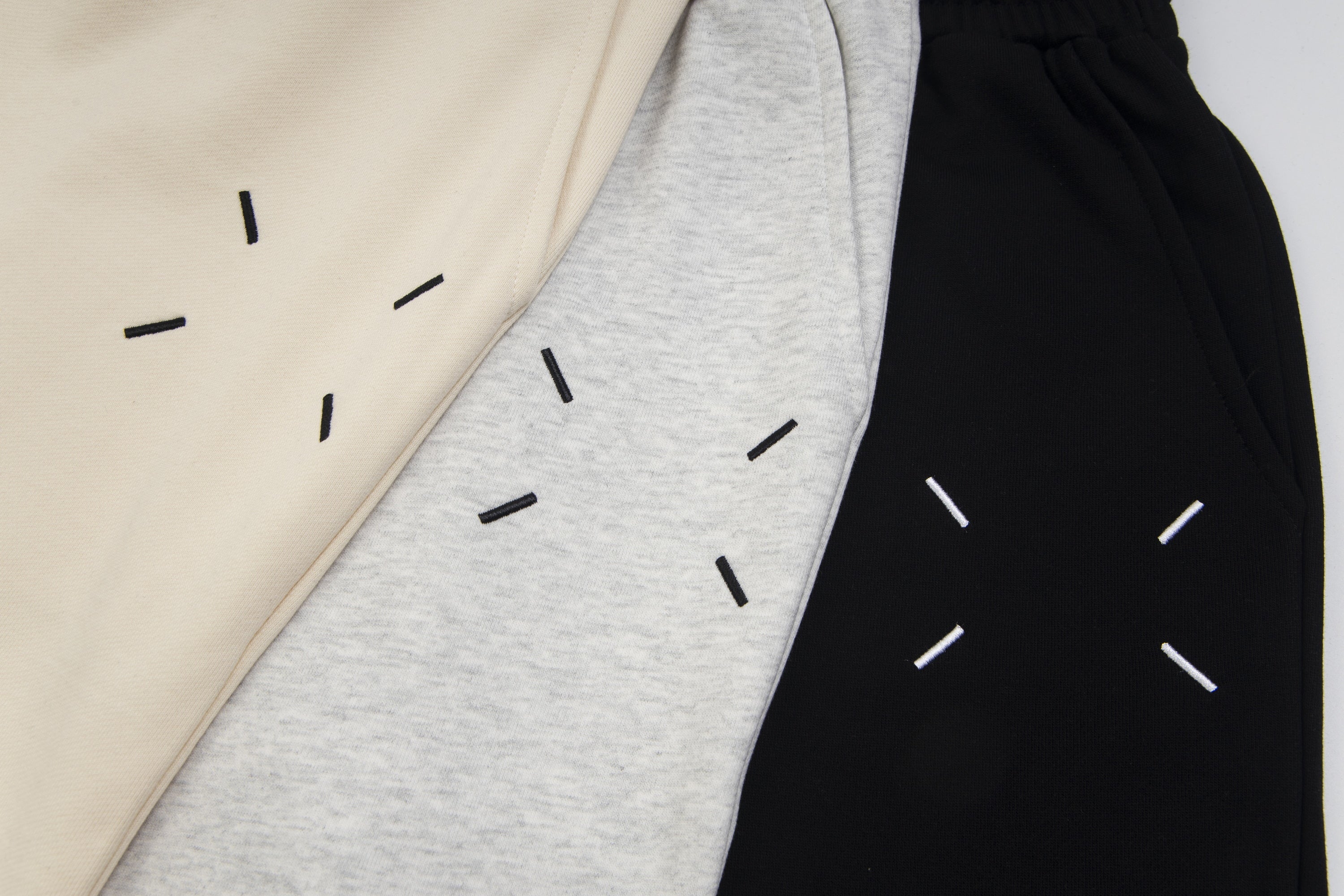 Side view of Maison Margiela shorts in beige, heather gray, and black with dash artwork.