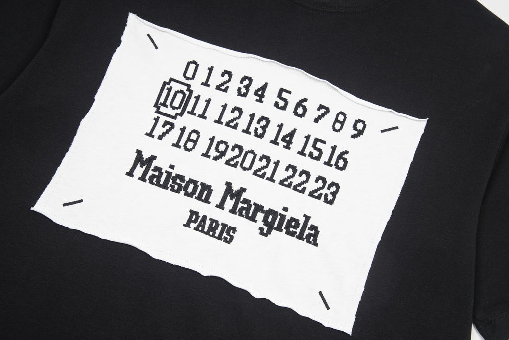 Black T-shirt close-up: white Maison Margiela number graphic on front patch