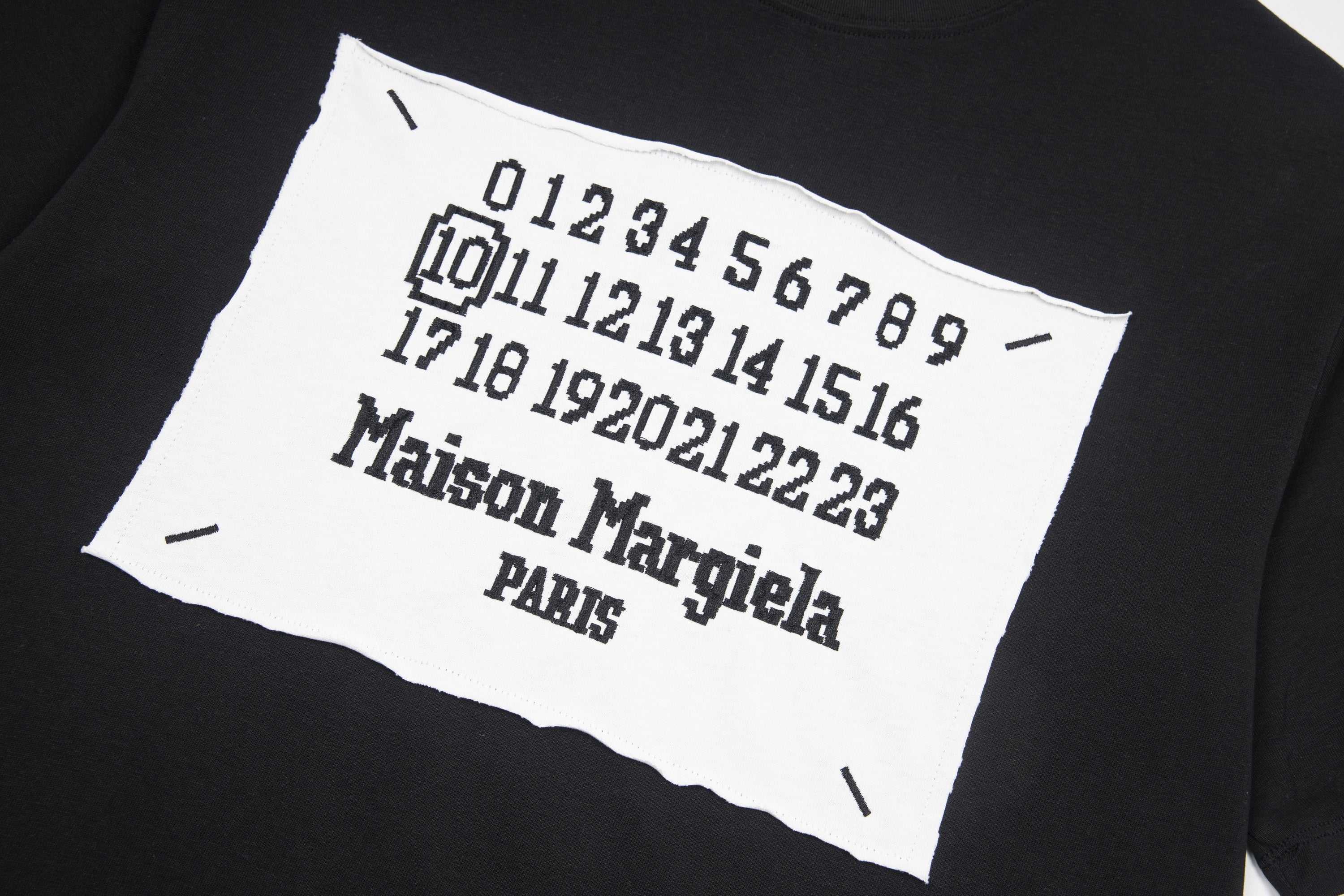 Black T-shirt close-up: white Maison Margiela number graphic on front patch