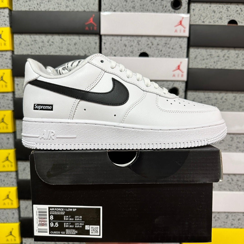White low-top sneakers with black swoosh and Supreme label, laid-on side view