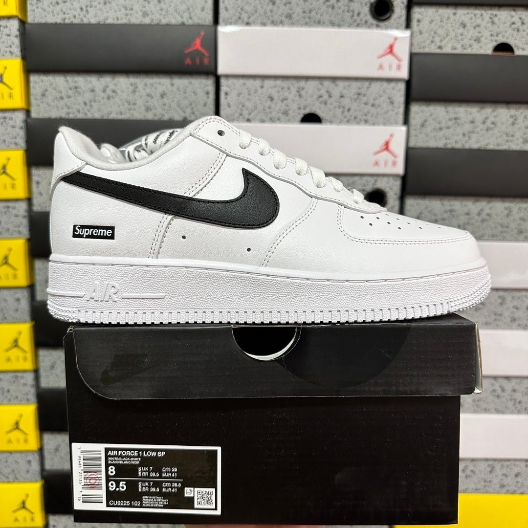 White low-top sneakers with black swoosh and Supreme label, laid-on side view