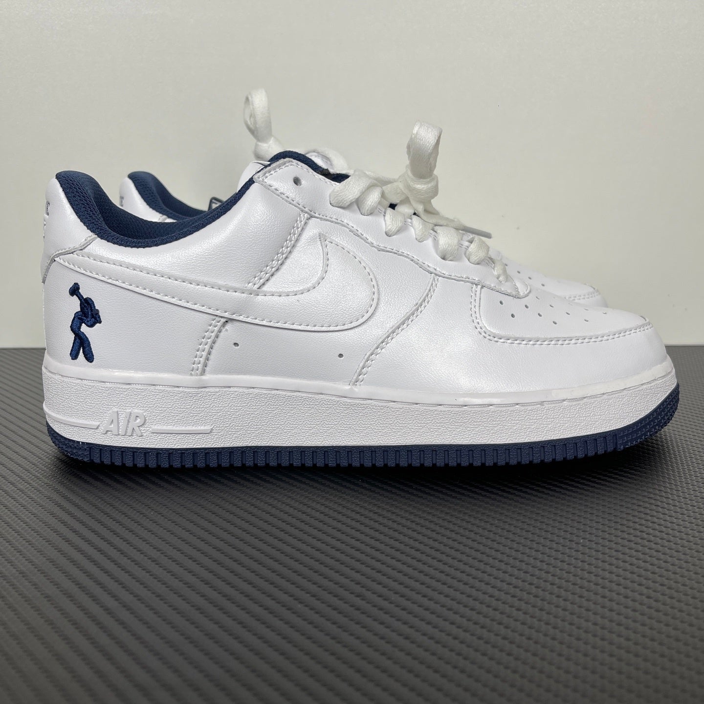 White Nike Air Force 1 sneaker with navy swoosh, heel logo, and lace-up upper