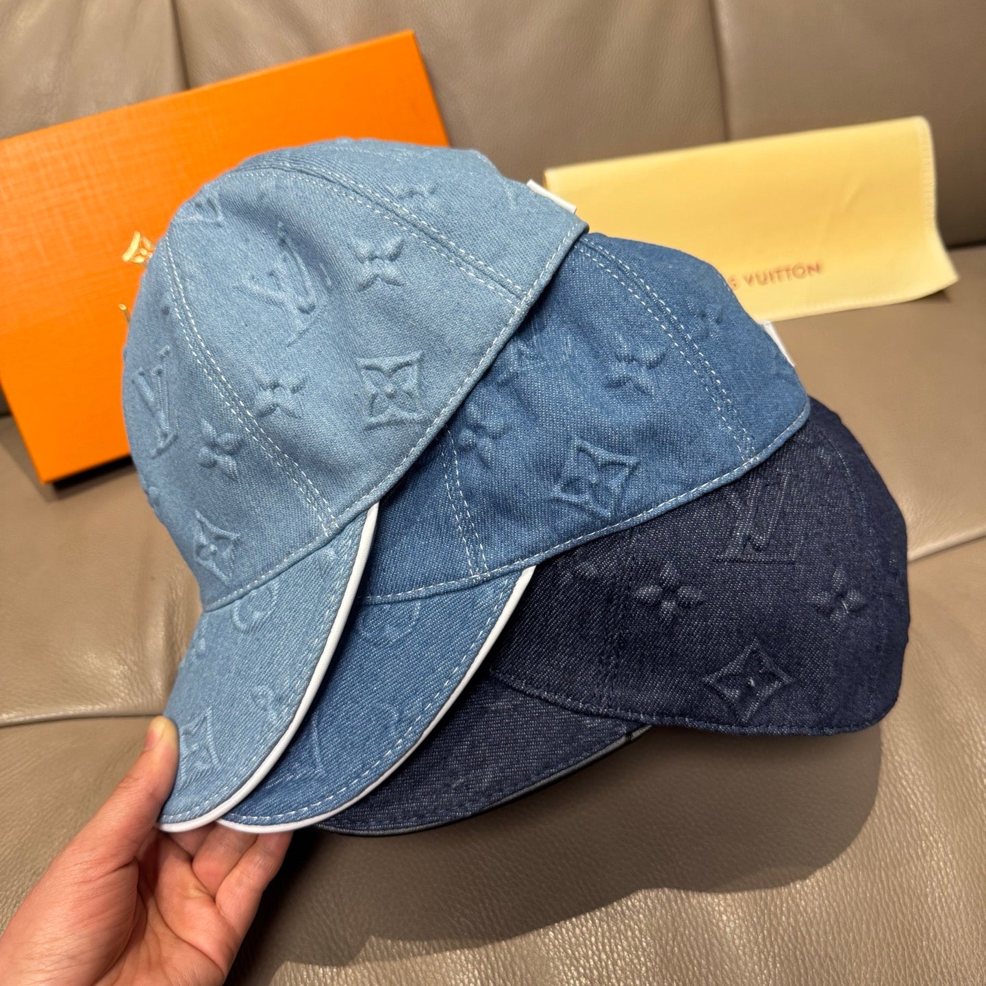 Two blue denim caps with embossed monogram motifs and curved brims