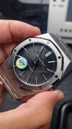 Audemars Piguet watch close-up with dark dial, raised markers, and date window at 21.