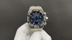 Stainless steel chronograph wristwatch with blue dial and bracelet, held on glove