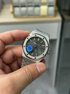 Audemars Piguet watch with grey dial, blue logo, textured case and steel bracelet