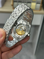 Audemars Piguet watch caseback with gold-toned movement, on metal bracelet.