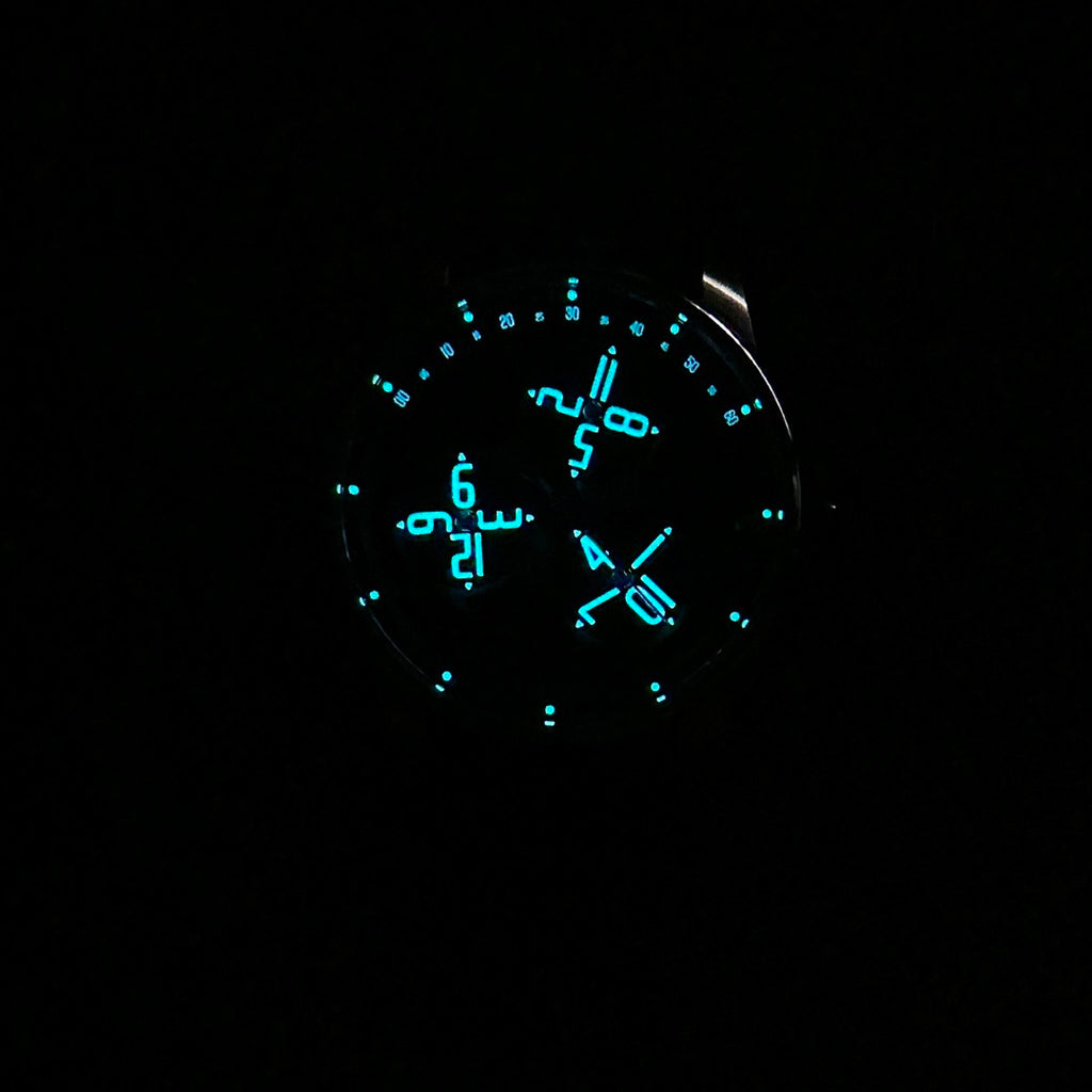 Round watch dial with glowing blue luminous numerals and hands on dark face