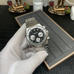 Audemars Piguet chronograph watch with black dial and steel bracelet, held in gloved hand