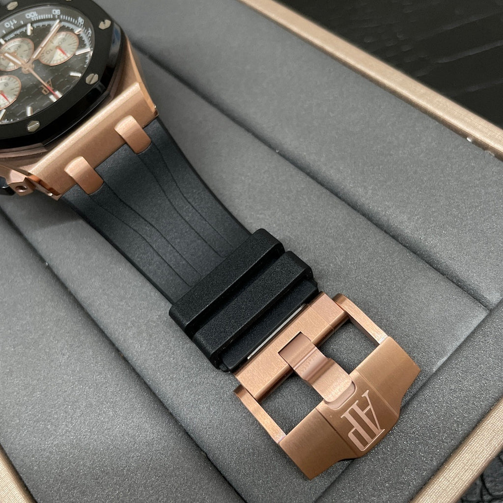 Rose gold watch clasp with black rubber strap shown close to the case