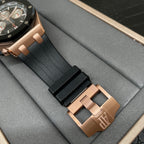 Rose gold watch clasp with black rubber strap shown close to the case