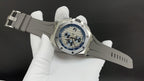 Stainless steel wristwatch on white strap, blue dial viewed at an angle