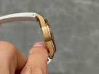 Rose gold-tone watch case side with screws and white rubber strap, angled view.