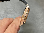 Rose-gold luxury wristwatch band link and black strap edge in side view.