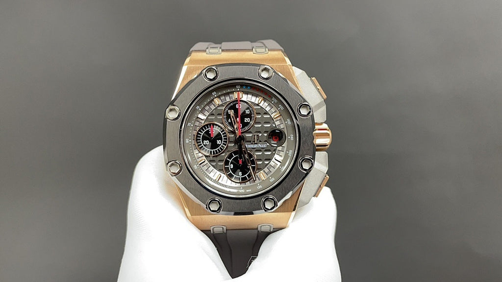 Octagonal luxury watch with dark dial, gold-tone bezel, and gray rubber strap